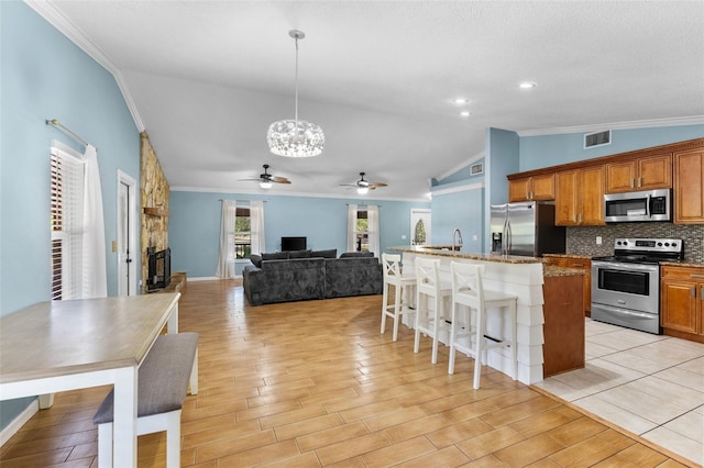 kitchen featuring decorative backsplash, ornamental molding, stainless steel appliances, decorative light fixtures, and lofted ceiling