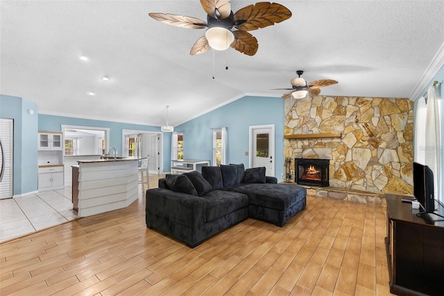 living room featuring ceiling fan, crown molding, sink, a fireplace, and lofted ceiling