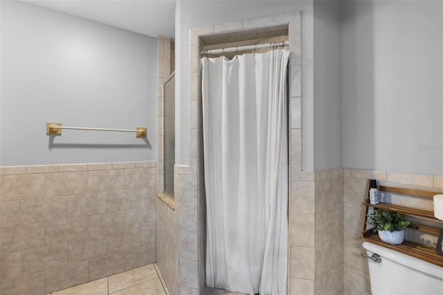 bathroom with toilet, a shower with curtain, tile patterned floors, and tile walls