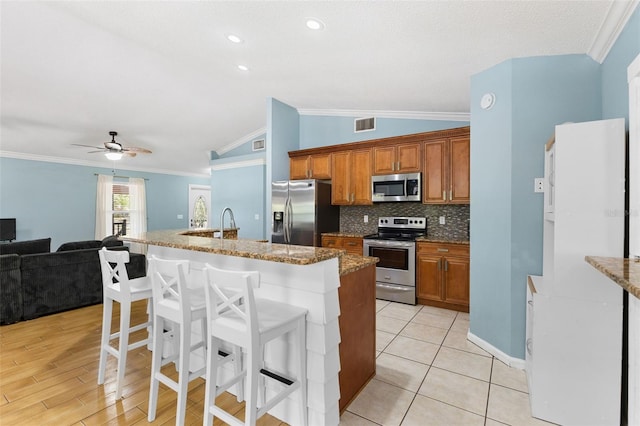 kitchen with a kitchen bar, stainless steel appliances, vaulted ceiling, ceiling fan, and a center island with sink