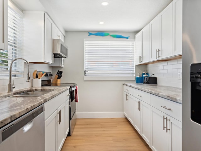 kitchen with sink, light hardwood / wood-style flooring, appliances with stainless steel finishes, light stone counters, and white cabinetry