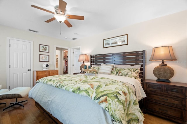 bedroom featuring a ceiling fan, a spacious closet, visible vents, and wood finished floors