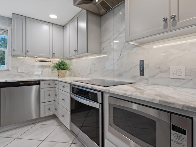 kitchen with wall chimney exhaust hood, light stone counters, decorative backsplash, and appliances with stainless steel finishes