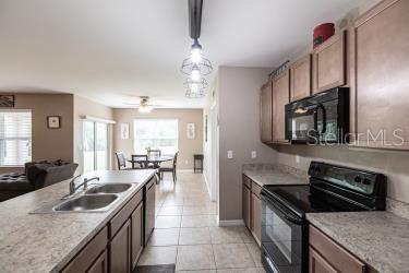 kitchen with light tile patterned flooring, ceiling fan, black appliances, pendant lighting, and sink