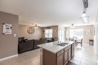 kitchen featuring sink, light tile patterned floors, ceiling fan, and an island with sink