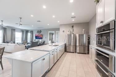 kitchen with white cabinetry, stainless steel refrigerator, ceiling fan, light stone countertops, and sink