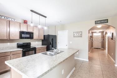 kitchen featuring hanging light fixtures, sink, black appliances, and an island with sink