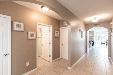 corridor featuring light tile patterned floors, arched walkways, and baseboards