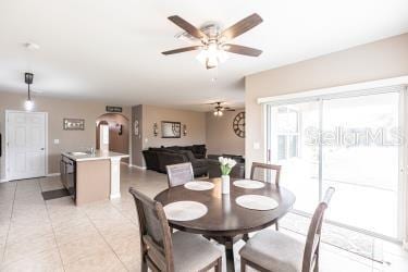 dining space with light tile patterned floors, arched walkways, and ceiling fan