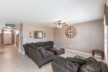 living area featuring a ceiling fan, arched walkways, baseboards, and light tile patterned floors