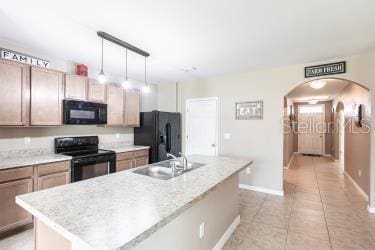 kitchen with light countertops, a sink, arched walkways, a kitchen island with sink, and black appliances