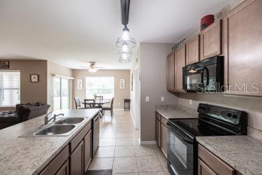 kitchen with light countertops, a ceiling fan, a sink, black appliances, and light tile patterned floors