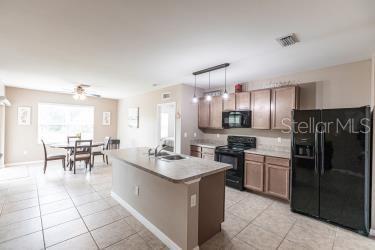 kitchen with light countertops, a sink, light tile patterned floors, black appliances, and ceiling fan