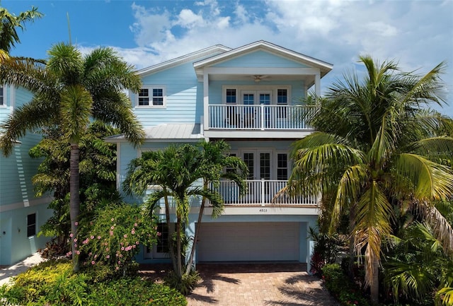 raised beach house featuring a balcony, a ceiling fan, an attached garage, french doors, and decorative driveway