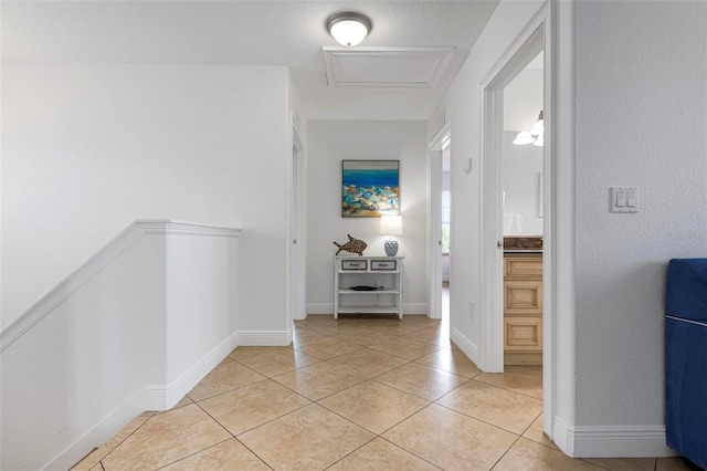 hallway with an upstairs landing, light tile patterned floors, attic access, and baseboards