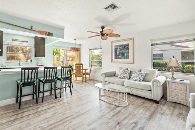 living room featuring ceiling fan, light hardwood / wood-style floors, and a textured ceiling