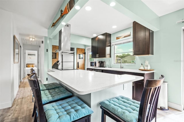 kitchen featuring a kitchen breakfast bar, sink, light wood-type flooring, island range hood, and dark brown cabinetry