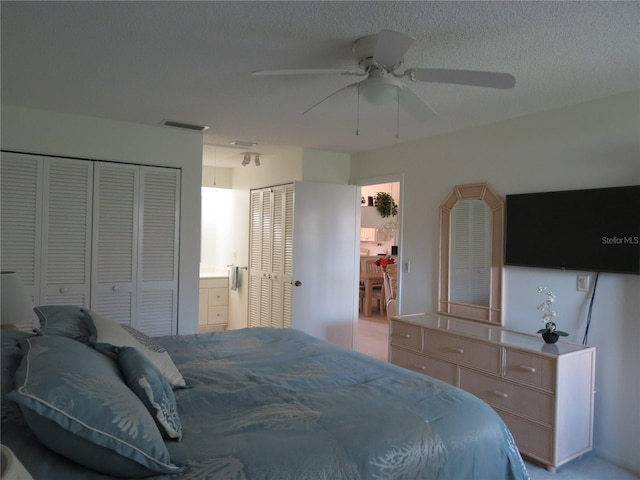 bedroom with a textured ceiling, ceiling fan, and two closets