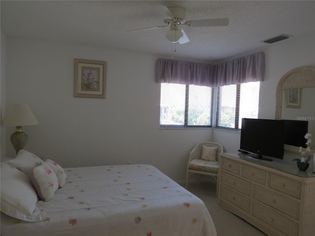 bedroom featuring ceiling fan, light colored carpet, and a textured ceiling