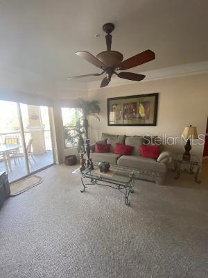 carpeted living room featuring ornamental molding and ceiling fan