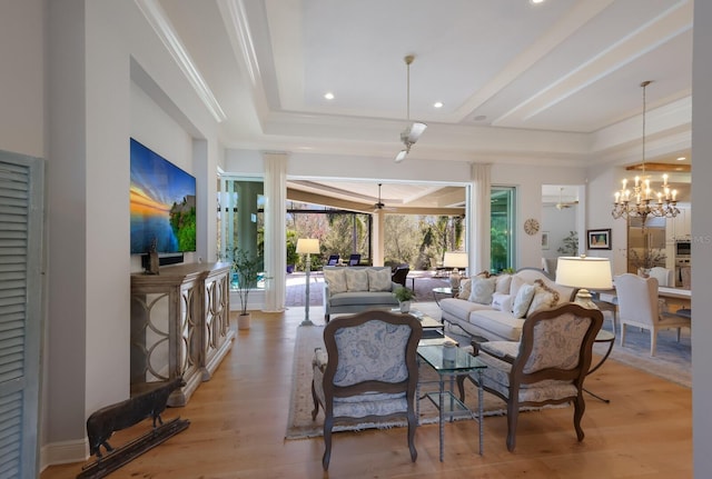 living room featuring ceiling fan with notable chandelier, a raised ceiling, and light hardwood / wood-style flooring