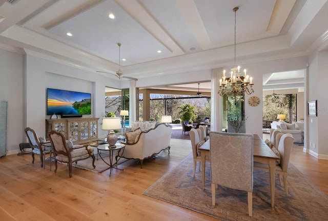 dining area with a raised ceiling, ceiling fan with notable chandelier, and light hardwood / wood-style flooring