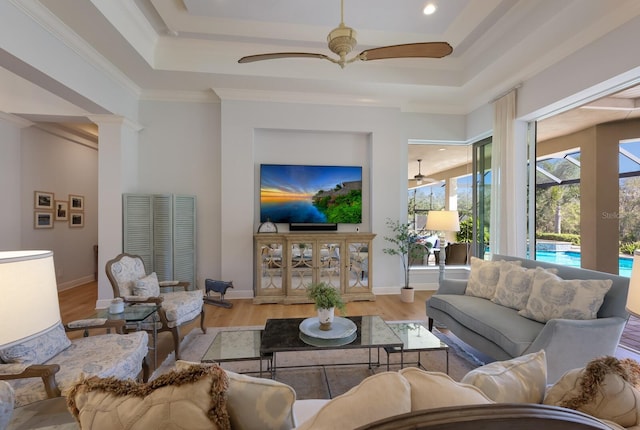 living room featuring a raised ceiling, ceiling fan, light hardwood / wood-style floors, and ornamental molding