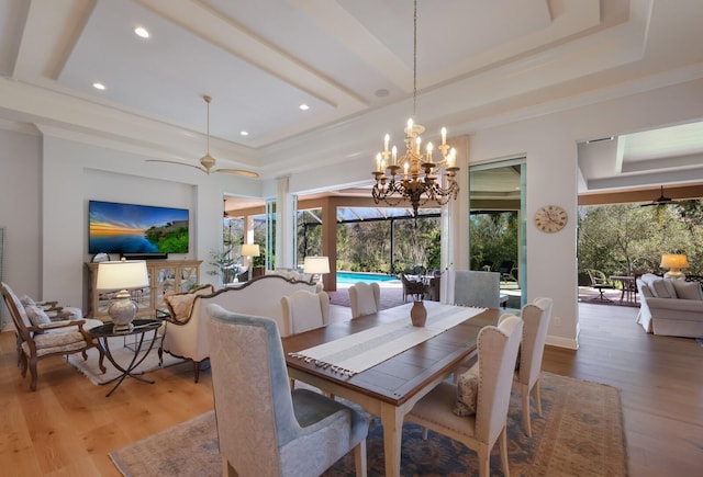 dining room with hardwood / wood-style flooring, plenty of natural light, ceiling fan with notable chandelier, and a tray ceiling