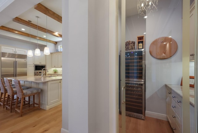 interior space featuring a kitchen breakfast bar, beverage cooler, built in appliances, decorative light fixtures, and light hardwood / wood-style flooring