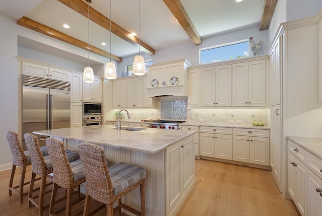 kitchen featuring tasteful backsplash, sink, built in appliances, beamed ceiling, and an island with sink