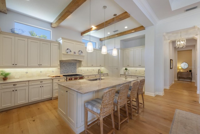 kitchen featuring decorative backsplash, light wood-type flooring, sink, beam ceiling, and a center island with sink