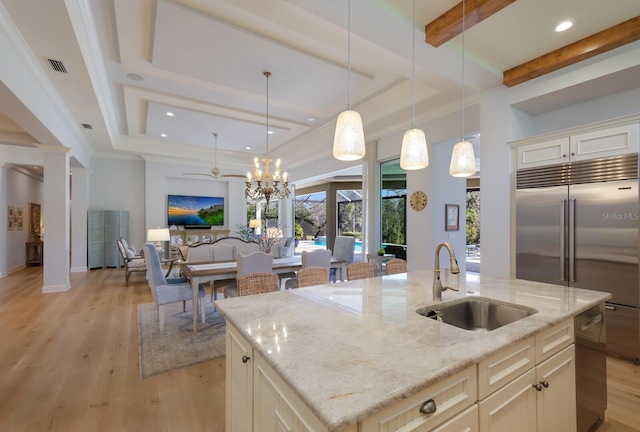 kitchen featuring sink, built in fridge, light stone counters, decorative light fixtures, and a center island with sink