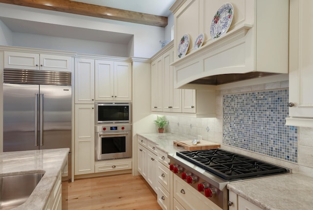 kitchen featuring beam ceiling, tasteful backsplash, light stone counters, built in appliances, and light wood-type flooring