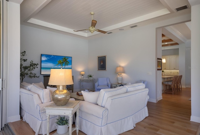 living room featuring light hardwood / wood-style floors, a raised ceiling, and ceiling fan