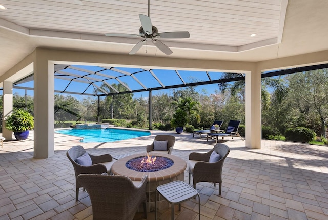 view of swimming pool with glass enclosure, ceiling fan, a fire pit, a patio area, and an in ground hot tub