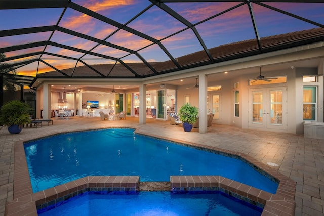 pool at dusk featuring glass enclosure, ceiling fan, a patio, and french doors