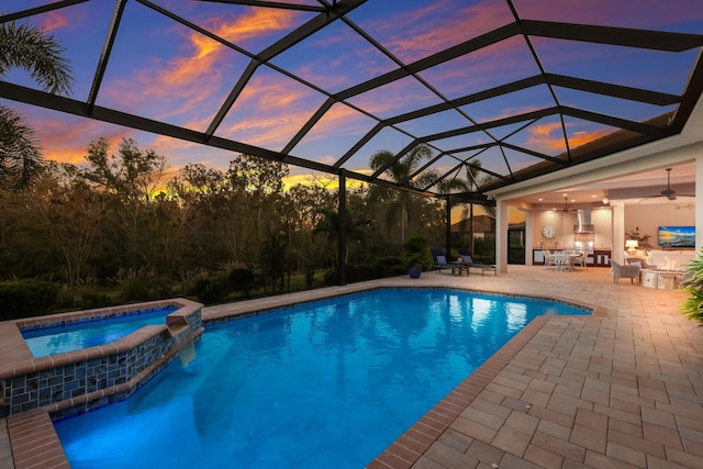 pool at dusk with glass enclosure, ceiling fan, an in ground hot tub, and a patio