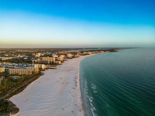 aerial view at dusk featuring a water view and a view of the beach