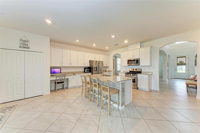 kitchen with sink, stainless steel appliances, a kitchen bar, a center island with sink, and white cabinets