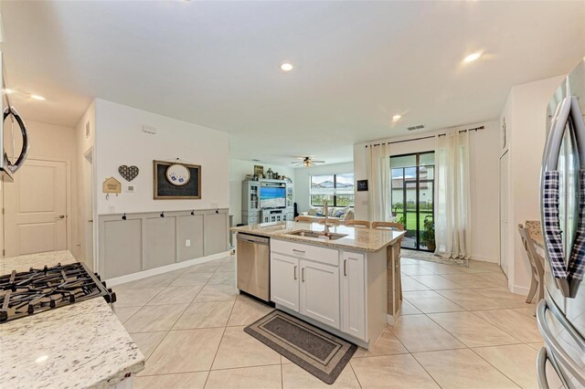 kitchen featuring a kitchen island with sink, white cabinets, ceiling fan, light stone counters, and stainless steel appliances