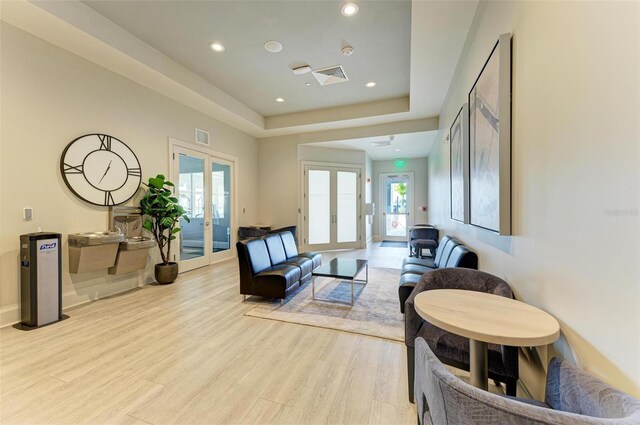 living room with a raised ceiling, a wealth of natural light, french doors, and light hardwood / wood-style floors