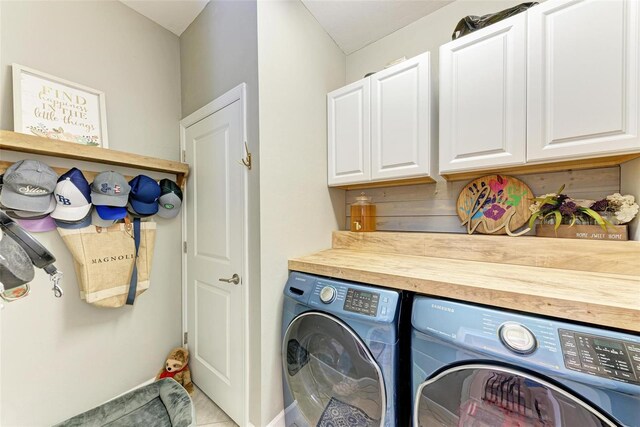 clothes washing area featuring cabinets, light tile patterned floors, and washing machine and dryer