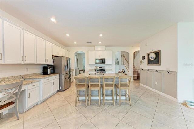 kitchen featuring light stone counters, a breakfast bar, white cabinets, a center island with sink, and appliances with stainless steel finishes