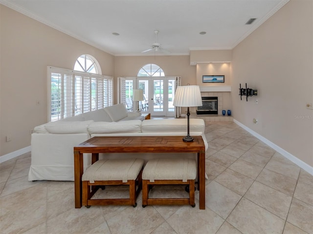 living room featuring a tiled fireplace, ceiling fan, crown molding, and light tile patterned flooring