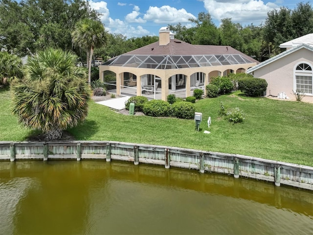 rear view of house featuring glass enclosure, a yard, and a water view