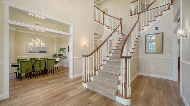 stairway featuring hardwood / wood-style flooring, ornamental molding, a notable chandelier, and a towering ceiling