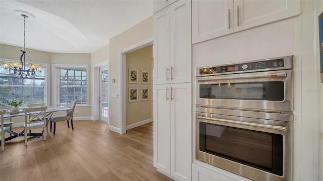 kitchen with stainless steel double oven, hanging light fixtures, a textured ceiling, white cabinets, and light hardwood / wood-style floors