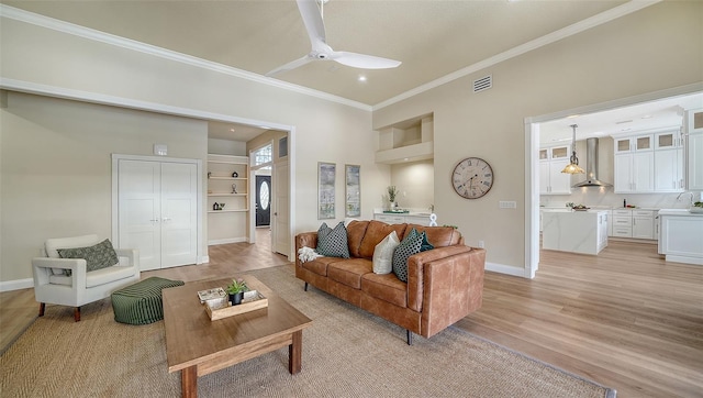 living room featuring ceiling fan, light wood-type flooring, crown molding, and built in features