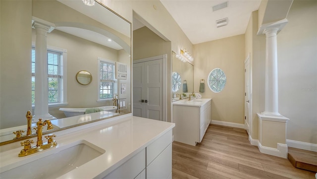 bathroom with a washtub, wood-type flooring, decorative columns, and vanity