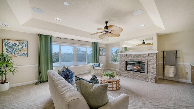 carpeted living room with a tray ceiling, ceiling fan, a textured ceiling, and a brick fireplace